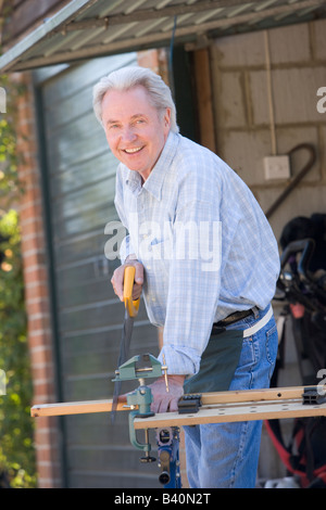 Man at shed sawing wood and smiling Stock Photo