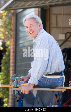 Man at shed sitting on tool bench smiling Stock Photo