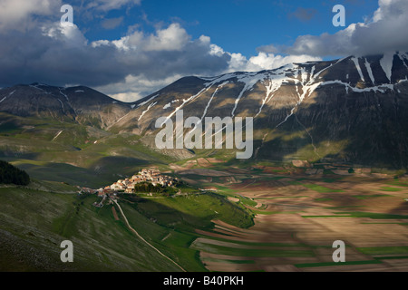 the village of Castelluccio perched above the Piano Grande with the mountains of Monti Sibillini National Park, Umbria, Italy Stock Photo