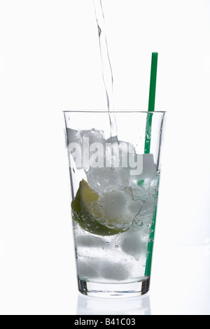 Glass with a slice of lime and ice cubes in it getting filled with water Stock Photo