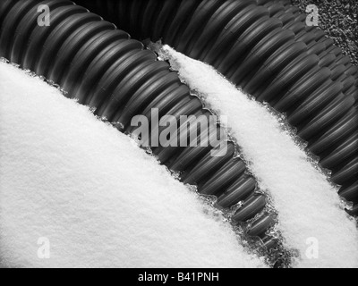 A round of coiled corrugated drain pipe partially covered in snow on asphalt. Stock Photo