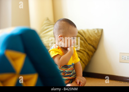 A sitting seven month old boy smiles as he looks at an electrical plug. Stock Photo