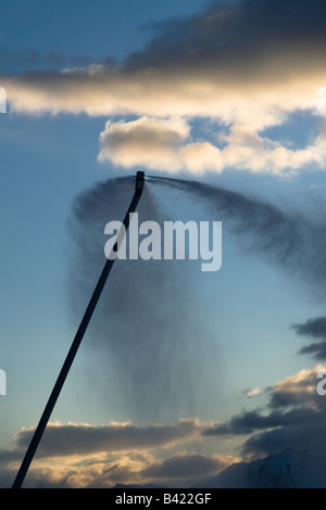 A plume of artificial snow from snow-making equipment in the French alps, against mountains and clouds in the background. Stock Photo