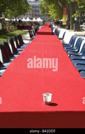 a lone plastic takeaway expresso cup sits on a long red empty table in a park in montpellier, France Stock Photo