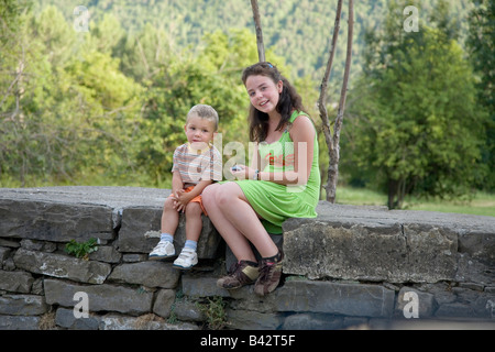 Pretty girl in green dress sitting with little brother on stone wall near Ainsa, Aragon, in the Pyrenees Mountains, Province of Stock Photo