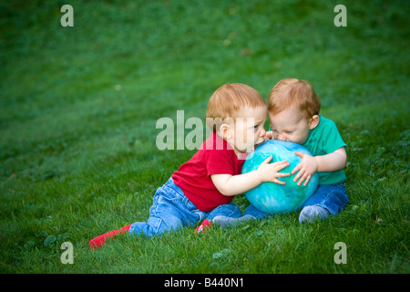 Young redheaded baby boys sitting outside on grass playing with ball Stock Photo