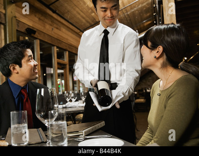 Asian waiter showing wine to couple Stock Photo