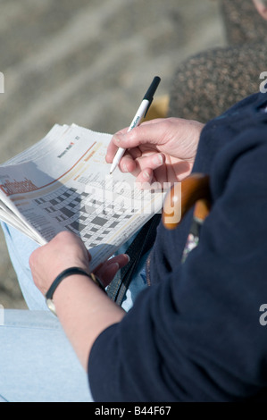 Person man completing a UK british newspaper crossword puzzle Stock Photo