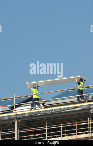 Two construction site workers carrying a panel of insulation material on building site Wales UK, summer blue sky Stock Photo