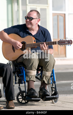 Smiling disabled man sitting in wheelchair playing 12 string acoustic guitar outdoors on sunny afternoon Stock Photo