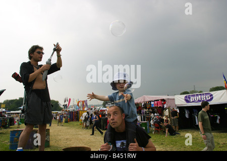 Glastonbury Music Festival  A  stallholder blows bubbles to attract the interest of a child being carried by his father Stock Photo