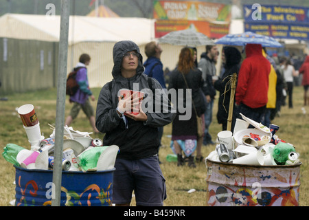 Woman carries beer  cups past full rubbish bins as genlr rain falls.  Glastonbury Music Festival 2003 Held on 1,000 acre Worthy Farm in Somerset, UK, over three days at the end of June almost every year since 1970, the festival now attracts a capacity crowd of 112,500.  This year festival tickets sold out in 18 hours. Stock Photo