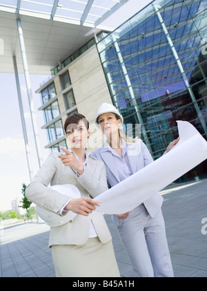 Germany, Baden-Württemberg, Stuttgart, two businesswomen with hard hats discussing building plan Stock Photo