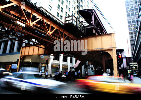 CARS PASSING AND PEOPLE CROSSING WELLST STREET UNDER EL TRAIN IN DOWNTOWN CHICAGO ILLINOIS USA DURING AFTERNOON RUSH HOUR Stock Photo