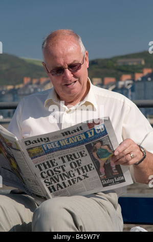 Middle aged man sitting outdoors reading the Daily Mail newspaper on a summer morning Stock Photo