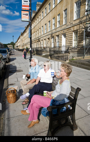 People having a tea picnic on bench in street Bath UK Stock Photo