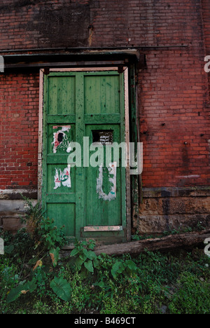 A battered green door makes a sharp contrast against a worn red brick wall.  Former Duquesne Brewery, South Side, Pittsburgh, PA Stock Photo