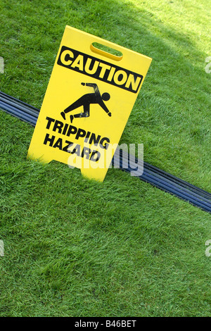 Caution Trip Hazard sign health and safety at work wires and cables across an outdoor grass lawn Stock Photo
