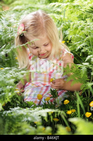 cute little blond girl picking yellow flowers in nature Stock Photo