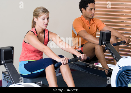 Woman on rowing machine and man making sit-ups on fitness ball at gym ...