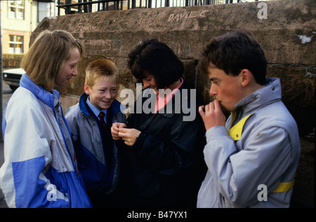 Young teenage boys and girls gather on a street corner to smoke, Glasgow Stock Photo