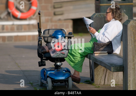 Woman with mobility scooter reading newspaper in the sunshine Aberaeron Ceredigion Wales UK Stock Photo