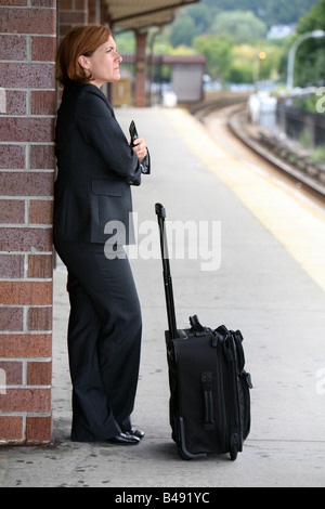 Commuting businesswoman keeps busy while awaiting the arrival of her train Stock Photo