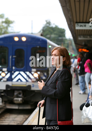 Commuting businesswoman keeps busy while awaiting the arrival of her train Stock Photo