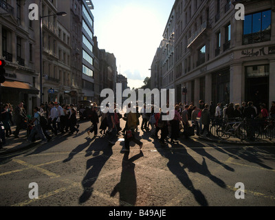 Many people shopping on Regent Street crossing one of the side streets in the afternoon sunlight London UK Stock Photo