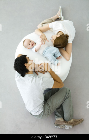 Parents and baby relaxing on ottoman, baby holding mother's hand, overhead view Stock Photo
