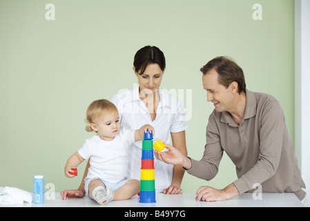 Toddler stacking plastic toys, parents watching Stock Photo