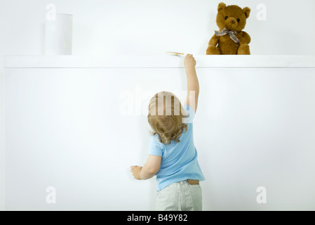 Toddler reaching for lollipop on high shelf, rear view Stock Photo