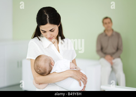 Woman holding sleeping baby, husband sitting in background Stock Photo