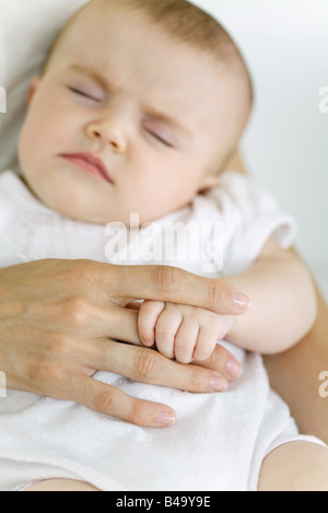 Baby sleeping, holding mother's finger, cropped view Stock Photo