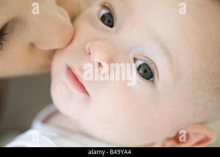 Infant looking at camera, mother kissing cheek, cropped