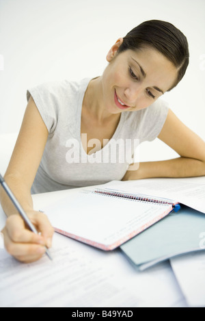 Woman sitting at desk, looking at document and writing in notebook Stock Photo