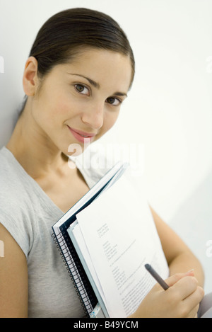 Young woman holding documents and notebook, smiling at camera Stock Photo