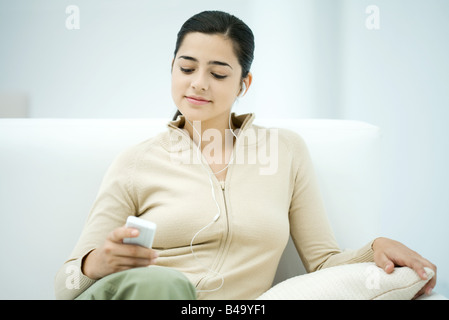 Young woman sitting on sofa, listening to MP3 player