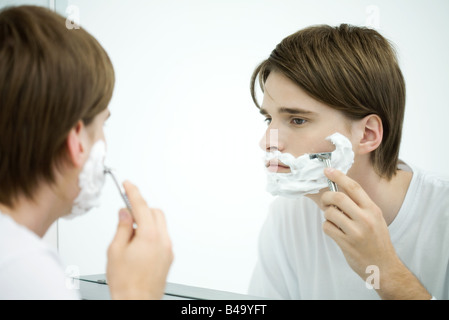 Young man looking at self in mirror, shaving Stock Photo
