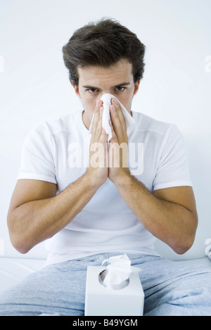 Man blowing his nose with a tissue, looking at camera Stock Photo