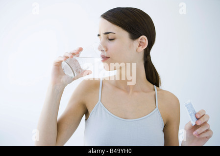 Woman drinking effervescent water, holding medicine packet Stock Photo