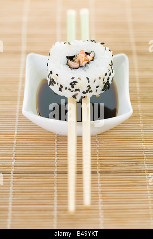 Maki sushi balanced on chopsticks over dish of soy sauce Stock Photo