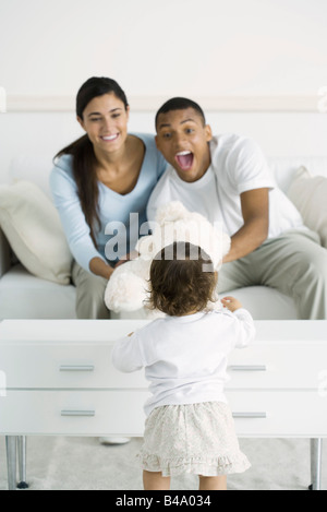 Parents giving toddler girl teddy bear, smiling Stock Photo