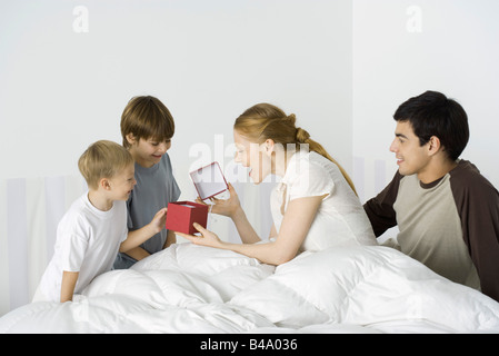 Two boys giving mother present in bed, husband watching Stock Photo