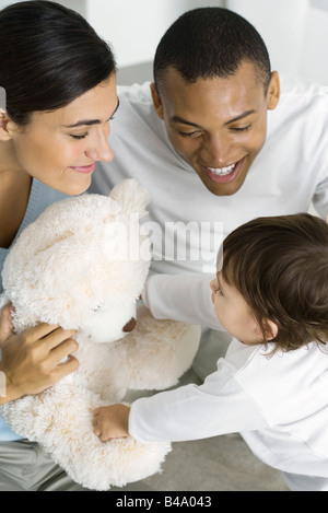 Parents giving toddler daughter a teddy bear, high angle view Stock Photo