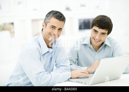 Two men using laptop computer together, both smiling at camera Stock Photo