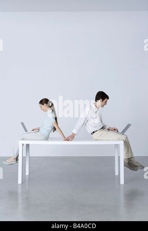 Couple sitting back to back, using laptop computers, holding hands Stock Photo