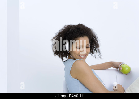 Woman listening to headphones connected to apple, eyes closed Stock Photo