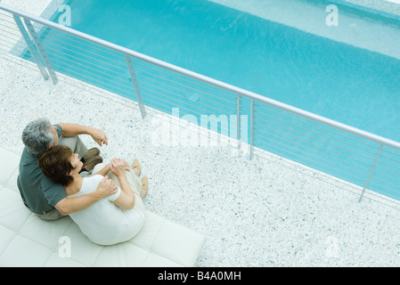 Husband and wife sitting by pool, his arm around her shoulder, her head on his Stock Photo