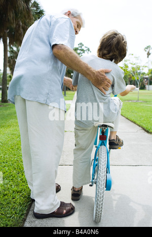 Senior man helping his grandson learn to ride a bicycle Stock Photo